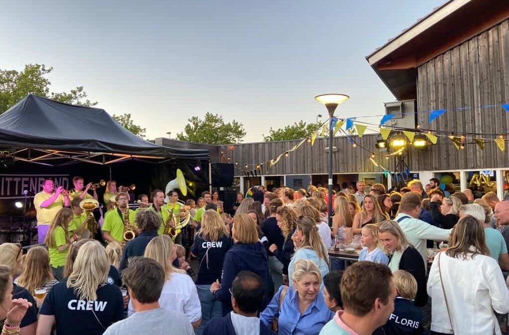 Blaaskapel Redelijk Onverantwoord staat op een podium en speelt voor een groep mensen van de hockey voor het 60 jarige jubileum